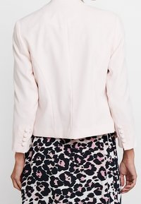 Jasnoróżowa, dopasowana marynarka z długimi rękawami, z guzikami przy mankietach. Nosi się ją na wzorzystą spódnicę w czarno-różowy wzór w cętki.