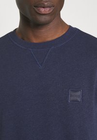 Sweatshirt azul-marinho em tecido texturizado com decote redondo e uma pequena etiqueta retangular preta com "BOSS" na parte da frente.