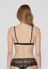 Schwarzer Spitzen-BH mit verstellbaren Trägern und einem Haken-und-Öse-Verschluss, kombiniert mit passenden schwarzen Unterhosen mit Spitzenbesatz.