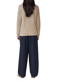 Beige strukturierter Strickpullover mit einer taillierten Passform und langen Ärmeln, kombiniert mit weiten dunkelblauen Jeans und hellen Schuhen.