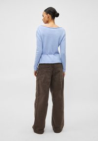Pull tricoté bleu clair avec un large décolleté, une taille cintrée et des manches longues, assorti à un pantalon cargo marron ample avec des poches arrière.