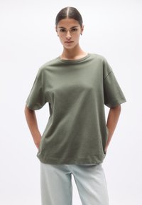 Tricou scurt din bumbac moale, de culoare verde măsliniu, cu guler rotund și croială lejeră, asortat cu blugi din denim deschis la culoare.