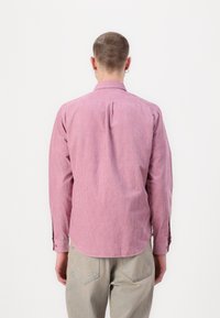 Long-sleeve shirt in light pink with a subtle striped pattern, featuring a standard collar and buttoned cuffs. Worn over light-colored pants.