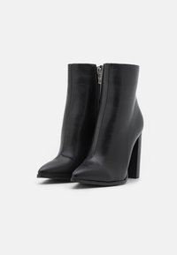 Bottes chelsea noires en cuir avec un bout pointu, fermeture éclair sur le côté et un talon carré. Texture lisse et design minimaliste.