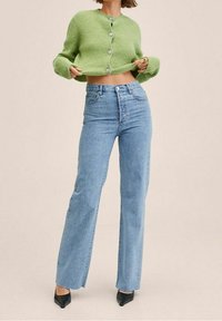 Hellgrüne, gerippte, kurze Strickjacke mit silbernen Knöpfen, kombiniert mit hoch taillierten, geraden blauen Jeans und schwarzen spitzen Pumps.