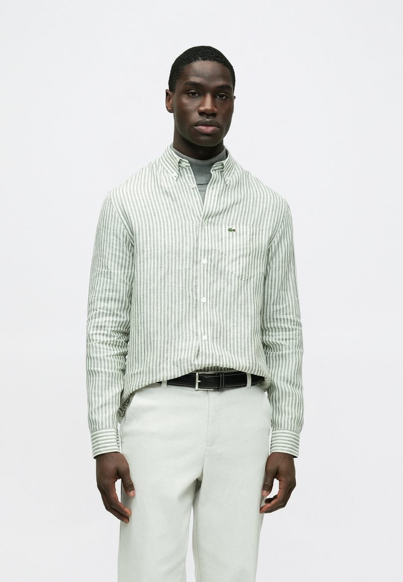 Zöld-fehér csíkos, gombos ing klasszikus gallérral, bal mellrészen zsebbel és apró logóval a mellkason. Világos nadrággal viselve.