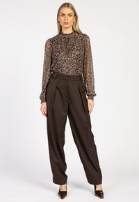 Transparante blouse met luipaardprint en hoge hals, gecombineerd met bruin geruite high-waisted broek en puntige bruine hakken.