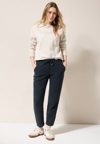 Lichtbeige sweatshirt met tekstdetail, gecombineerd met gestructureerde marineblauwe broeken met een elastische tailling en zakken. Casual schoenen.