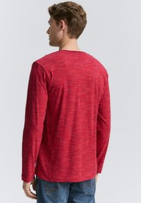 Rød skjorte med lange ærmer i et tekstureret, meleret mønster, rundt halsudskæring og lige kant. Stoffet virker blødt og let.