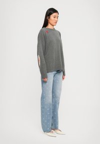 Gray sweater with oversized fit, ribbed cuffs, and side slits, paired with light blue jeans featuring small pink floral patterns.