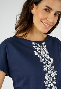 Camiseta de algodón azul marino con estampado floral blanco en un lado, escote redondo y mangas cortas. Textura suave, ajuste casual.