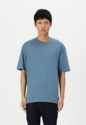 T-shirt bleu à coupe décontractée, manches courtes, col rond, en coton lisse, associé à un jean foncé, design minimaliste, sans motifs visibles.