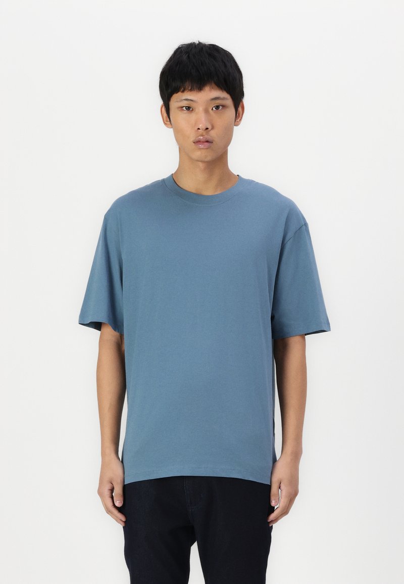 Camiseta azul de corte relajado, mangas cortas, cuello redondo, fabricada en algodón suave, combinada con jeans oscuros, diseño minimalista, sin patrones visibles.