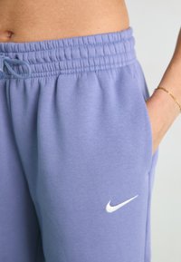 Svijetloplave trenirka s vezicom u struku, s bijelim Nike logotipom. Tkanina je mekana s vidljivom teksturom i bočnim džepovima.