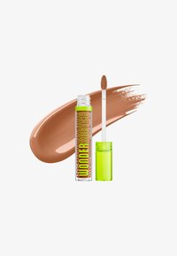 Tube de correcteur avec bouchon vert néon et applicateur en baguette montrant un échantillon de crème beige moyen sur fond blanc.