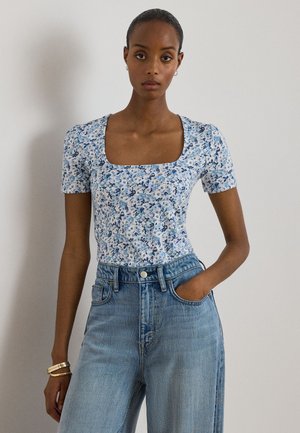 Γυναίκα που φοράει μπλε και λευκό μπλουζάκι με κοντά μανίκια και τετράγωνη λαιμόκοψη, μαζί με ανοιχτό μπλε τζιν παντελόνι ψηλόμεσο και φαρδύ, με το ένα χέρι στην τσέπη.