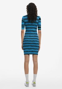 Abito lavorato a maglia con strisce orizzontali blu e nere, maniche corte, silhouette aderente e taglio a ginocchio. Calzini e scarpe bianchi in vista.
