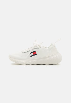 Biały niskoprofilowy sneaker z dzianiny, białe sznurówki, gruba teksturowana podeszwa oraz prostokątne logo "Tommy Jeans" w kolorach czerwonym, białym i czarnym z boku.