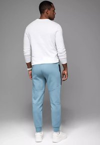 Jasnoniebieskie dresy z bocznymi kieszeniami i czarnym zamkiem, w połączeniu z białą koszulą z długim rękawem oraz białymi sneakerami.