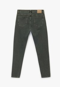Jeans ajustados en denim de color verde oliva oscuro con una textura suave, que presentan bolsillos traseros y un parche de cuero beige en la cintura.