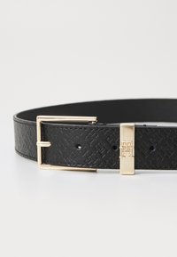 Ceinture en cuir noir avec un motif texturé, dotée d'une boucle en métal doré et d'un accent gravé sur le côté.