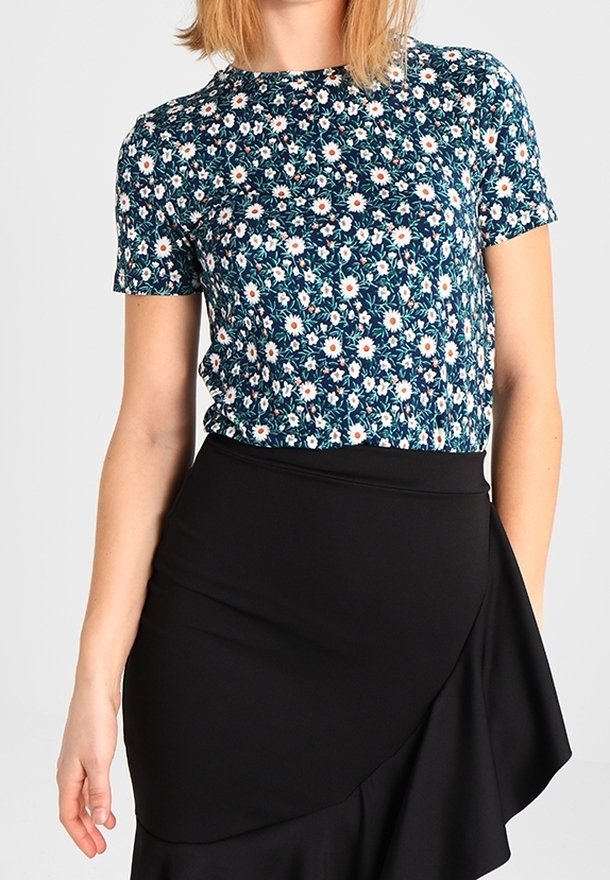 Květinový top s krátkým rukávem na námořnickém pozadí, zdobený bílými sedmikráskami a zelenými listy, doplněný černou zavinovací sukní s texturovaným povrchem.