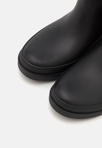 Bottes de pluie noires avec une texture lisse, un bout rond et une semelle en caoutchouc striée pour une bonne adhérence. Le design est minimaliste avec une silhouette élégante.