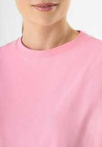 Roze katoenen T-shirt met een ronde hals en korte mouwen. Heeft een subtiele geborduurde bloemdesign op de linkerkant van de borst. Soepele textuur.