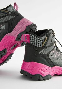 Bottes de randonnée noires et roses avec une tige texturée, étiquette HydroGuard et une semelle extérieure en caoutchouc durable avec un motif de semelle robuste.