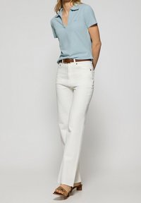 Light blue polo shirt with a v-neck and short sleeves, paired with white straight-leg jeans and brown heeled sandals with a decorative strap.