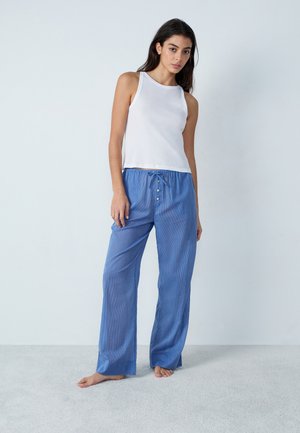 Un débardeur blanc sans manches et un pantalon de pyjama bleu à rayures avec taille réglable par cordon et accents de boutons, sur un fond clair.