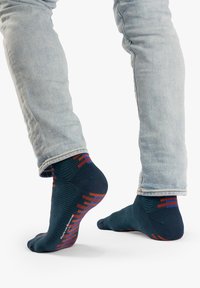 Calcetines azul marino con patrones geométricos rojos y naranjas, textura acanalada y talón reforzado, combinados con jeans azul claro.