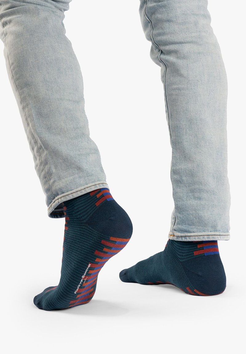 Calcetines azul marino con patrones geométricos rojos y naranjas, textura acanalada y talón reforzado, combinados con jeans azul claro.