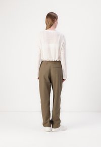 Lightweight, long-sleeve white top with a loose fit, paired with olive green trousers featuring a relaxed silhouette and back pocket detail.