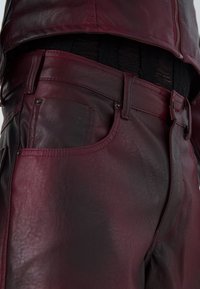 Bordo kožnate hlače s glatkom teksturom, detaljnim šavovima i klasičnim dizajnom s pet džepova. Prilagođen struk s suptilnim sjajem.