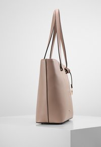 Jasnoróżowa torba na ramię o teksturowanej powierzchni, czarnych rączkach, złotych elementach metalowych oraz z zapięciem na sznurek. Charakteryzuje się smukłym, strukturalnym kształtem.