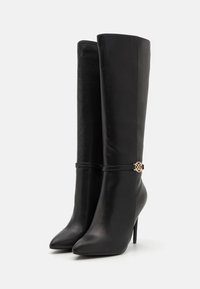 Bottes en cuir noires montantes jusqu'aux genoux, à bouts pointus, talons aiguilles, avec une fine sangle ornée d'une petite boucle décorative dorée.