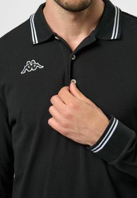 Černé polo tričko s texturovanou tkaninou, bílým pruhovaným límečkem a vyšitým logem Kappa na hrudi. Obsahuje značení na tři knoflíky.