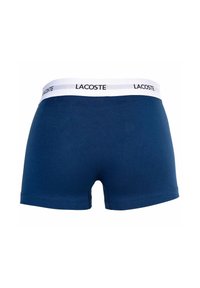 Námorníckomodré boxerky vyrobené z bavlny. Majú biely elastický pás s logom "Lacoste", hladkú textúru a priliehavý strih.