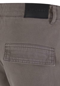 Un pantalon en coton gris présente une surface texturée, une étiquette en faux cuir au niveau de la ceinture et une seule poche arrière cousue.