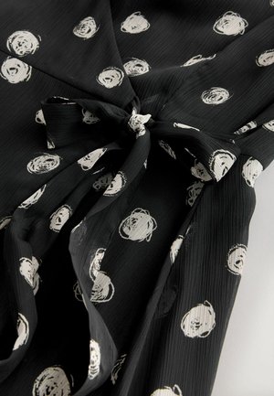 Schwarzes Musterkleid mit weißen kreisförmigen Designs, strukturiertem Stoff und gebundenem Taillendetail. Verfügt über einen V-Ausschnitt und eine fließende Silhouette.