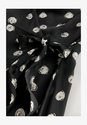 Schwarzes Musterkleid mit weißen kreisförmigen Designs, strukturiertem Stoff und gebundenem Taillendetail. Verfügt über einen V-Ausschnitt und eine fließende Silhouette.