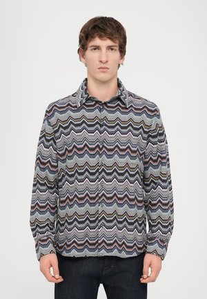Button-up shirt featuring a zigzag pattern in multiple colors: navy, pink, green, and white. Made of woven fabric with a collared neckline.