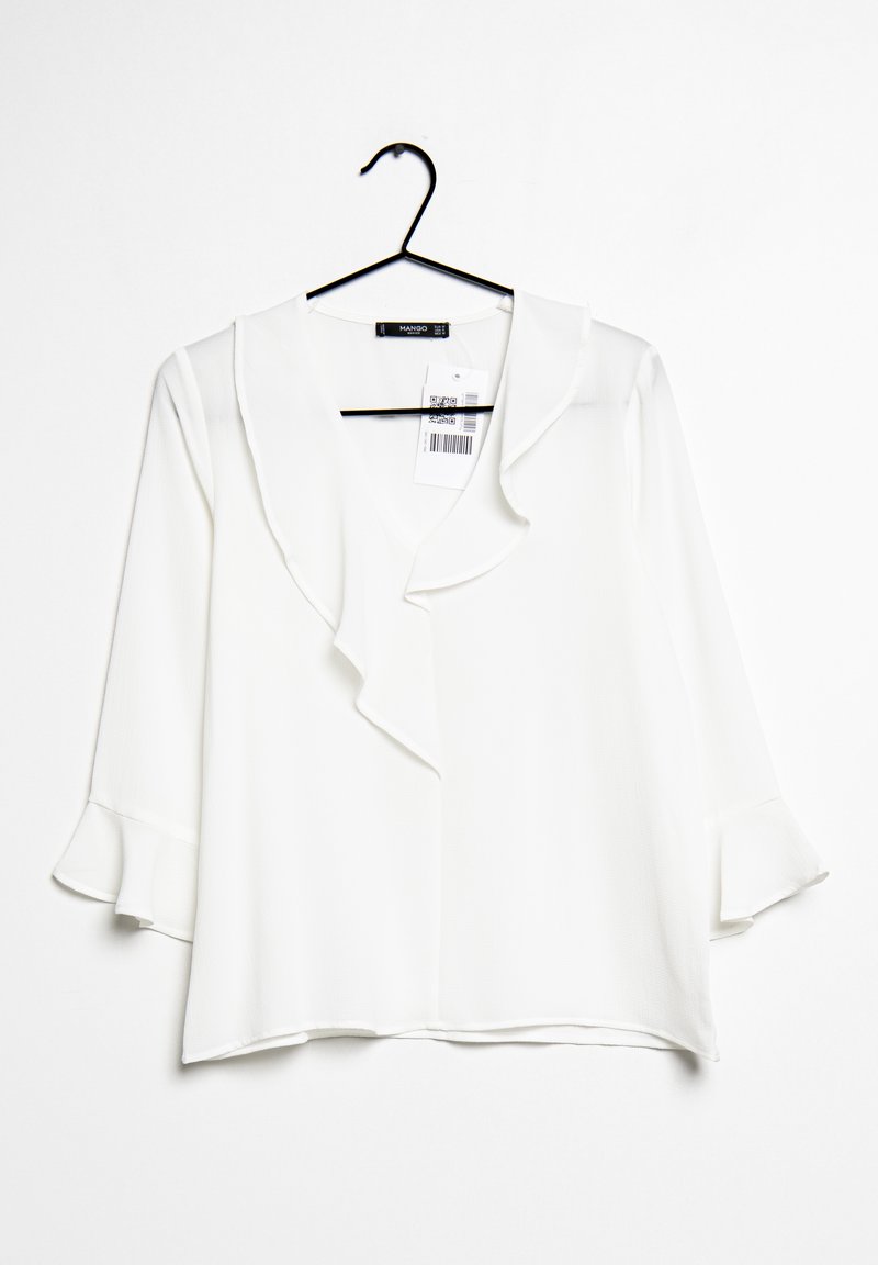 Blouse blanche à manches longues avec col et poignets à volants, suspendue sur un cintre noir devant un fond blanc avec une étiquette de prix visible.