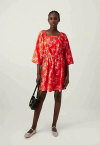 Punase lilleline kleit ruudu kaelusega, puffvarrukatega ja elastse vöökoha ning sobitatud musta kotiga ja valgete espadrillidega.