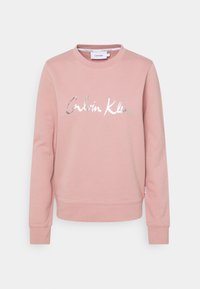 Felpa rosa con colletto girocollo, maniche lunghe, polsini a coste e logo "Calvin Klein" in argento metallizzato sulla parte anteriore. Morbido cotone misto.