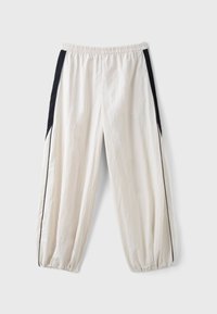 Pantalon de survêtement blanc ample avec panneaux noirs et fines rayures noires le long des côtés extérieurs, taille élastique et poignets élastiques aux chevilles.