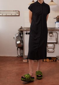 Czarna sukienka na guziki z krótkimi rękawami, z kołnierzykiem i dwiema przednimi kieszeniami. Połączona z oversize'owymi klapkami w czarno-zieloną tygrysią kratę.