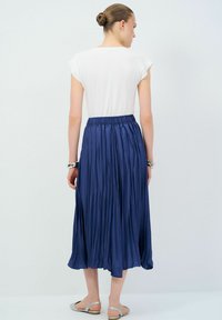 Jupe plissée navy avec taille élastique, en matériau léger et soyeux, associée à un haut blanc ajusté et des sandales plates en argent.