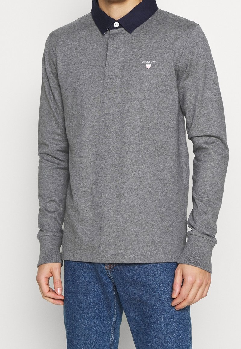Langärmliges graues Poloshirt mit einem marineblauen Kragen, ausgestattet mit einem kleinen Logo auf der Brust und gerippten Bündchen. Hergestellt aus einem weichen, strukturierten Stoff.